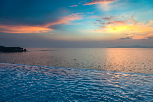 Hermosa vista de la piscina infinita con puesta de sol en el mar al atardecer.