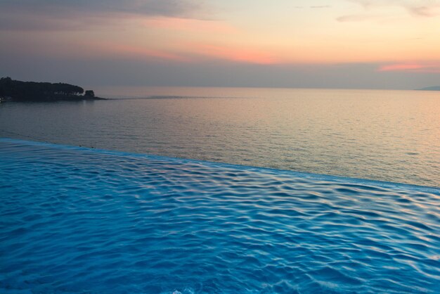 Hermosa vista de la piscina infinita con puesta de sol en el mar al atardecer.