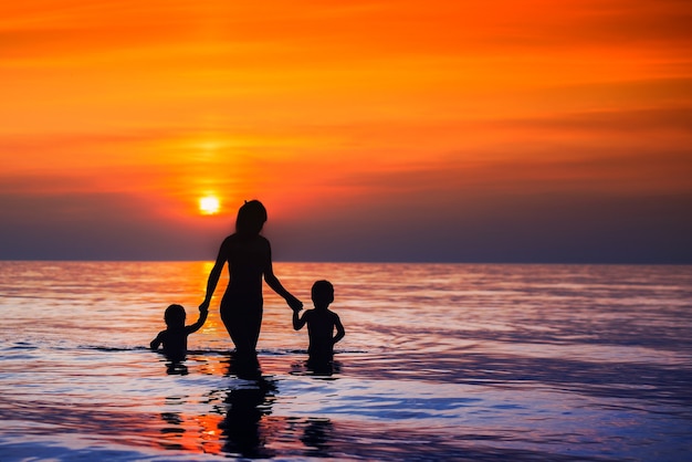 Hermosas al atardecer siluetas de madres con hijos caminando desde el mar hasta la orilla