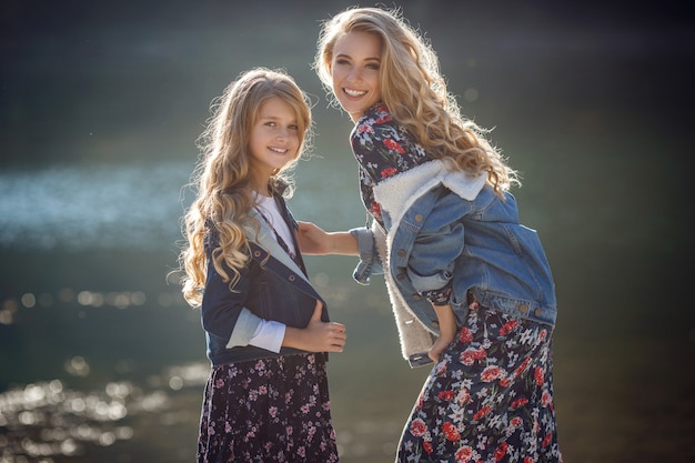 Hermosas amigas con estilo cerca de un lago de montaña en el bosque, estilo denim. La idea y el concepto de una infancia feliz, hermandad y unidad con la naturaleza.