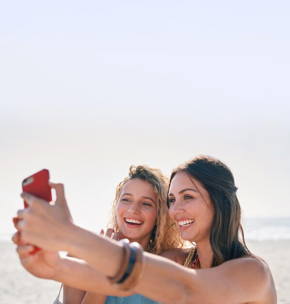 Hermosas amigas tomando fotos usando la cámara del teléfono inteligente en la playa sonriendo felices compartiendo vacaciones en las redes sociales