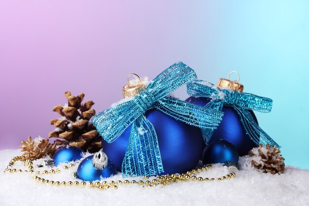 Hermosas bolas de Navidad azules y conos en la nieve sobre fondo brillante