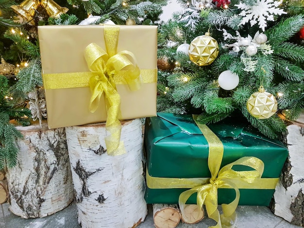 Hermosas cajas envueltas en papel dorado con regalos de Navidad en un tocón de abedul cerca de la Navidad