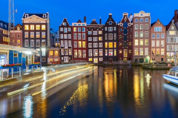 Hermosas casas de baile típicas holandesas y barcos turísticos en el canal Damrak de Amsterdam en la noche, Holanda, Países Bajos.