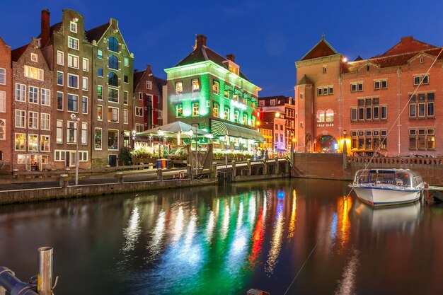 Hermosas casas de baile típicas holandesas y barcos turísticos en el canal Damrak de Amsterdam en la noche, Holanda, Países Bajos.