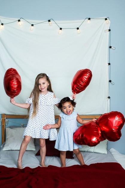 Hermosas chicas, blancas y de piel oscura, celebran el día de san valentín. globos de papel de aluminio rojo en forma de corazón