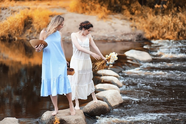 Hermosas chicas jóvenes en vestidos cruzan el arroyo en otoño