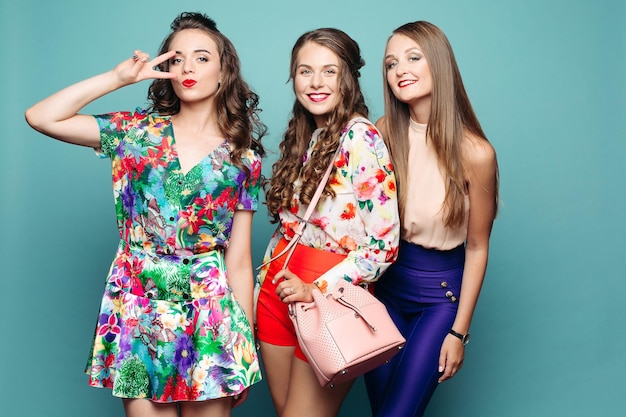 Hermosas chicas de moda con ropa brillante sonriendo a la cámara contra un fondo azul