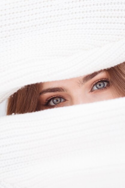 Foto hermosas chicas ojos azules entre dos mangas de suéter de lana blanca, retrato creativo.