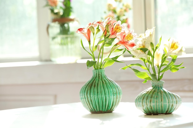 Hermosas flores de Alstroemeria en jarrones de aguamarina en el fondo de la ventana