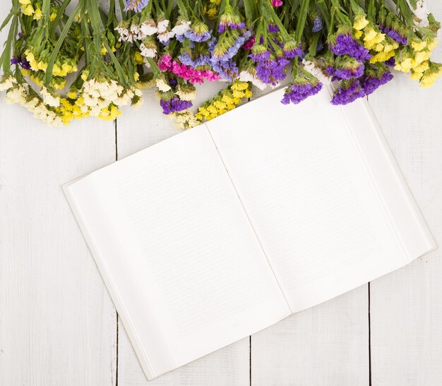 Hermosas flores de colores y libro en blanco abierto sobre una madera blanca