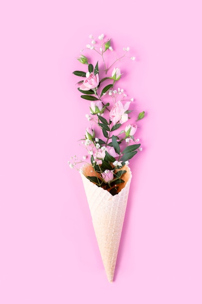 Hermosas flores en cono de helado sobre fondo rosa. Endecha plana