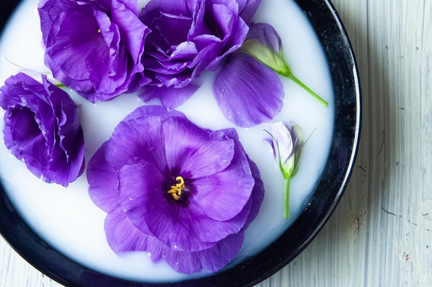 Hermosas flores de eustoma púrpura artificial en una placa negra con leche sobre fondo de madera