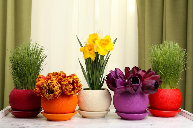 Hermosas flores con hierba verde en macetas sobre fondo de tela