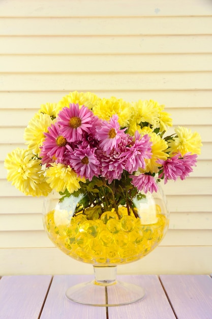 Foto hermosas flores en jarrón con hidrogel sobre mesa sobre fondo de madera