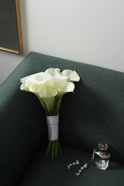 Hermosas flores de lirio de cala atadas con una botella de perfume y aretes en el sofá interior