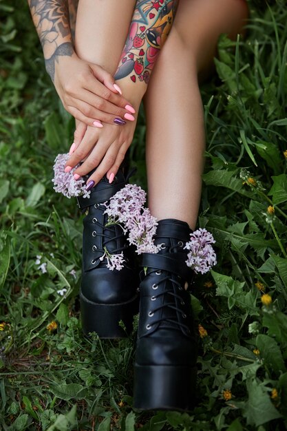 Hermosas flores en manos de una niña con tatuajes, cosméticos. Flores de verano y maquillaje brillante en las uñas de la mano de la mujer. Manicura y uñas rosas.