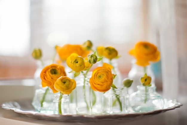 Hermosas flores naranjas de ranunculus en botellas antiguas y jarrones sobre una bandeja de plata antigua Ramos pequeños o regalos