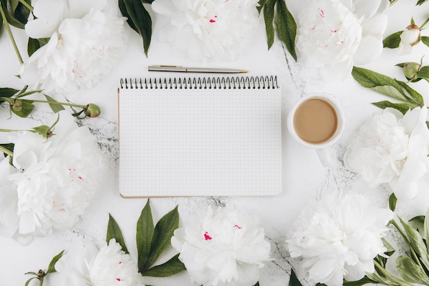 Hermosas flores de peonía blanca con cuaderno vacío en el espacio de copia de fondo de piedra de mármol blanco para su texto o diseño vista superior plana