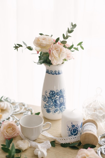 Hermosas flores rosas delicadas en un jarrón de porcelana blanca con un patrón gzhel en la decoración de una boda o cena