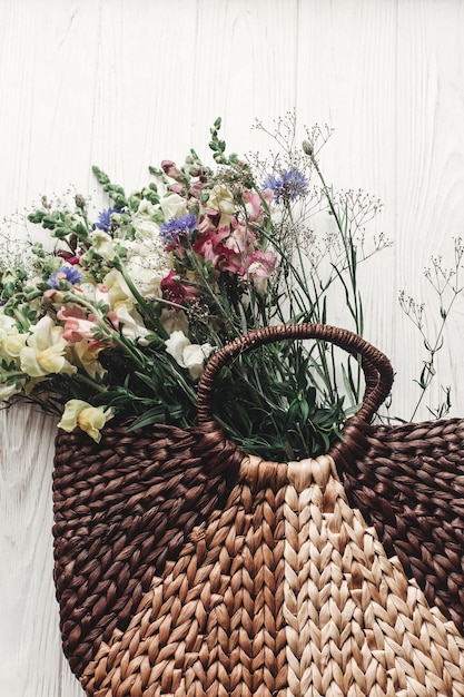 Foto hermosas flores silvestres en una bolsa de mimbre sobre un fondo de madera blanca rústica planas y coloridas flores en una canasta en un espacio claro para texto vista superior momento atmosférico rural imagen de verano