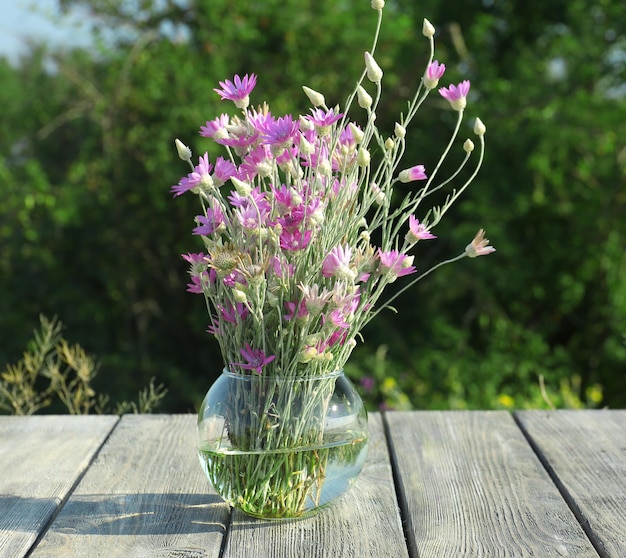 Hermosas flores silvestres en un jarrón sobre una mesa de madera en el fondo del campo