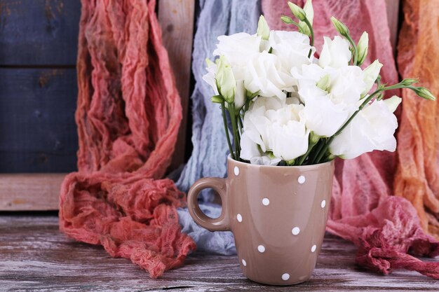 Hermosas flores en taza sobre fondo de tela