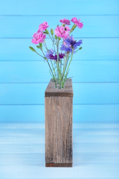 Foto hermosas flores de verano en jarrón sobre fondo de madera azul