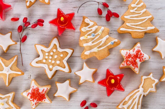 Hermosas galletas de jengibre de Navidad en glaseado blanco en forma de copos de nieve de abeto y estrellas Bayas rojas y velas sobre fondo de madera