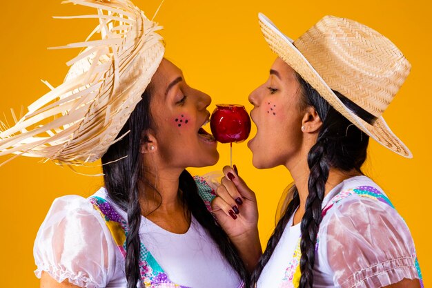 Hermosas gemelas en ropa de fiesta de junio comiendo una manzana de caramelo