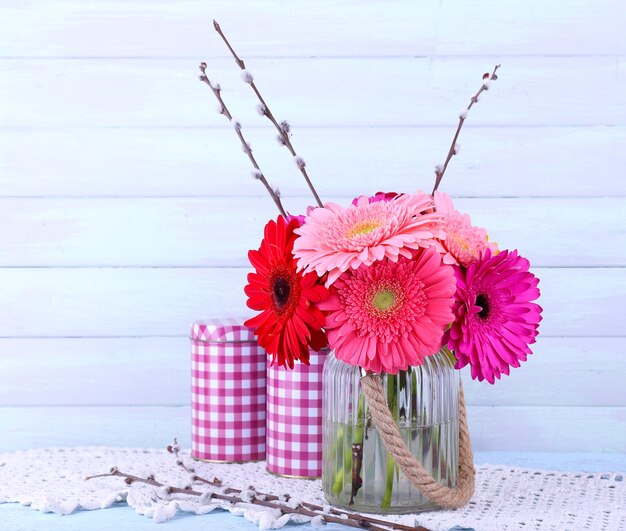 Hermosas gerberas brillantes en florero sobre superficie de madera