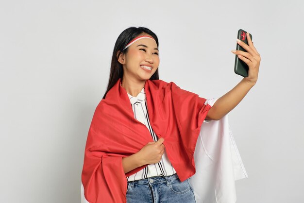 Foto hermosas jóvenes asiáticas celebran el día de la independencia de indonesia mientras hacen selfies en un celular aislado de fondo blanco