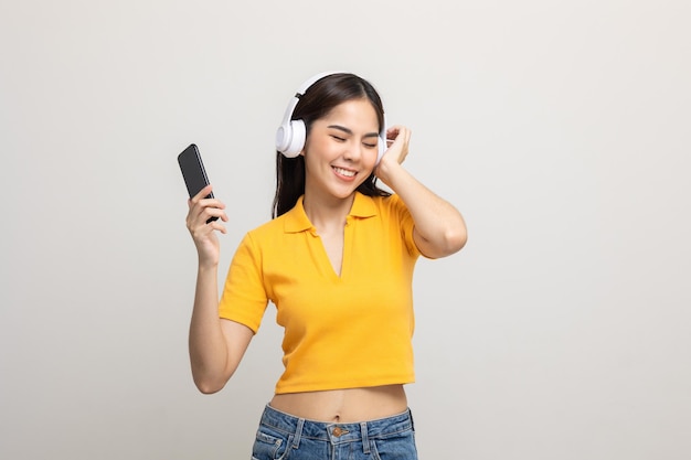 Hermosas jóvenes asiáticas eligen canciones y reproducen música desde la conexión de un teléfono inteligente con auriculares inalámbricos divirtiéndose en casa. Una adolescente escucha la música y disfruta relajándose en un fondo aislado.