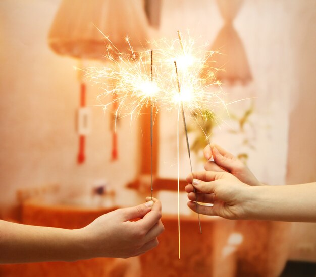 Hermosas luces de Bengala en manos de mujer en el fondo de la habitación