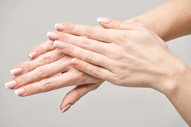 Foto hermosas manos femeninas con manicura francesa sobre superficie gris claro