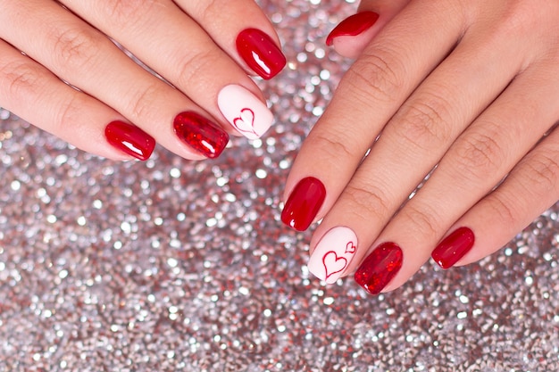 Hermosas manos femeninas con manicura roja, diseño de corazones, sobre fondo plateado