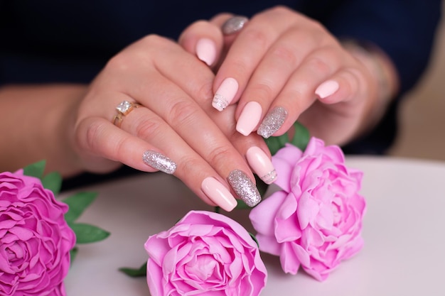 Foto hermosas manos femeninas con manicura rosa y peonías.