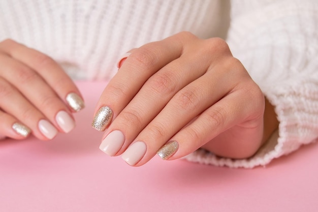 Hermosas manos femeninas con uñas de manicura beige sobre fondo rosa