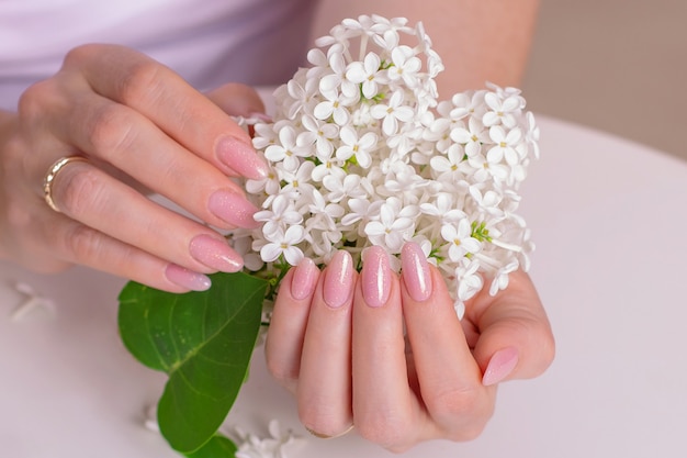 Hermosas manos femeninas con uñas de manicura esmalte de gel rosa y flores blancas