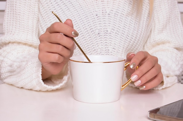 Hermosas manos femeninas con uñas de manicura festivas sosteniendo una taza de té