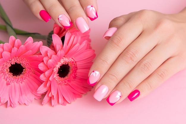 Hermosas manos femeninas con uñas de manicura románticas, esmalte de gel rosa, diseño de flores de gerbera