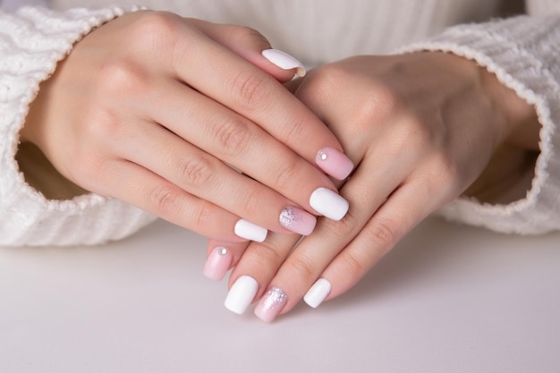 Hermosas manos femeninas con uñas de manicura rosas y plateadas sobre fondo blanco.