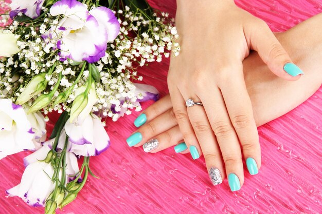 Foto hermosas manos de mujer con manicura azul cerca de un ramo de hermosas flores en un fondo de color