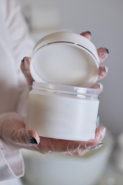 Hermosas manos de mujer sosteniendo un tubo de plástico de botella blanca con flores de primavera en blanco