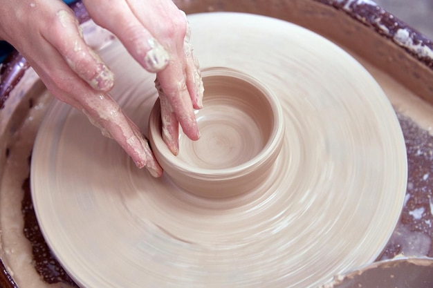 Hermosas manos de mujeres hacen platos de cerámica en un torno de alfarero giratorio de enfoque suave