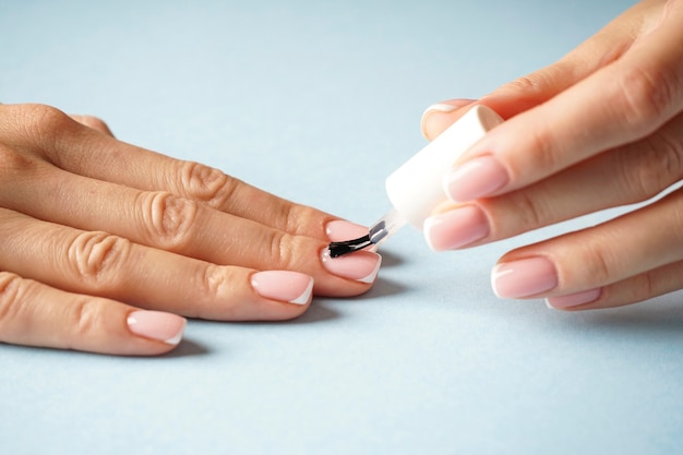 Hermosas manos de una niña con hermosa manicura sobre un fondo azul. Manicure francés.