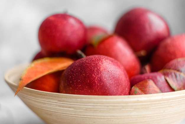 Hermosas manzanas rojas frescas con hojas de otoño en un jarrón de madera sobre una mesa de hormigón ligero. Temporada de cosecha