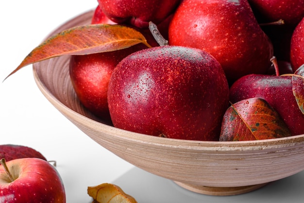 Hermosas manzanas rojas frescas con hojas de otoño en un jarrón de madera sobre una mesa de hormigón ligero. Temporada de cosecha