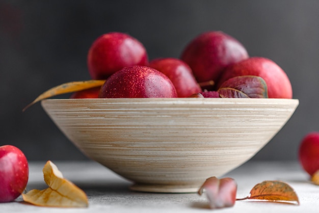 Hermosas manzanas rojas frescas con hojas de otoño en un jarrón de madera sobre una mesa de hormigón ligero. Temporada de cosecha