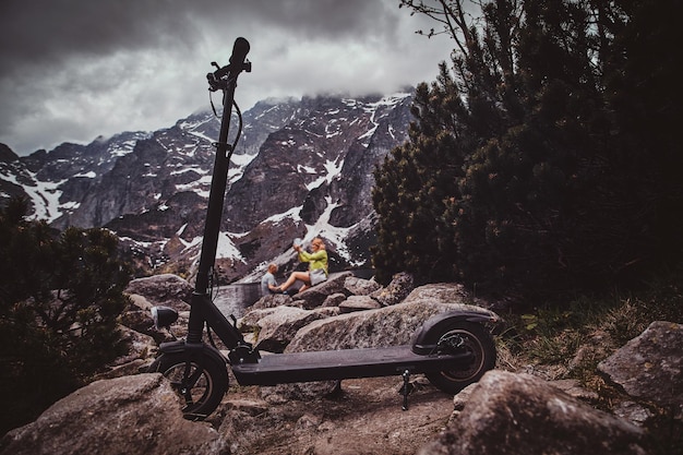 Hermosas montañas, nubes bajas y sombrías, piedras, pinos y scooter al frente.